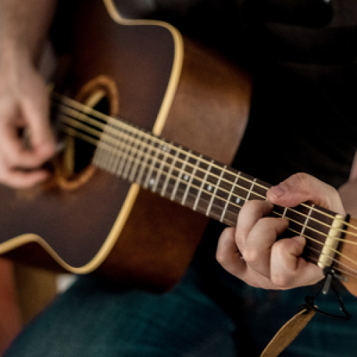 Someone is playing an acoustic guitar, focusing on their hands and the strings for a close-up view of the musical performance.