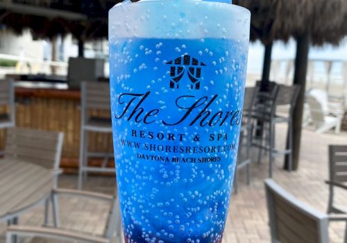 A hand holds a red and blue layered drink with a blue shark toy on top in a branded cup from 