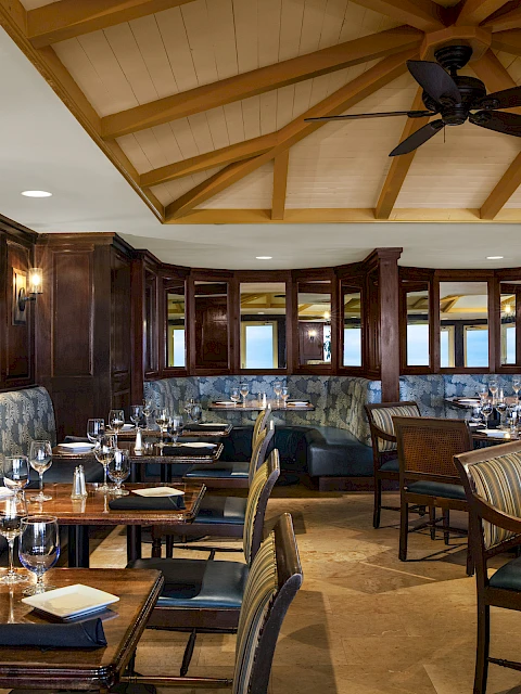 A sophisticated restaurant with elegant wooden furniture, large windows, and neatly set tables for dining.
