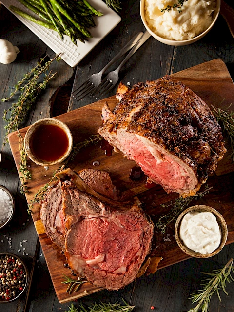 A cooked, sliced beef filet mignon with sides of mashed potatoes, gravy, and grilled asparagus on a dark wooden table.
