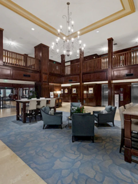 A spacious, elegant lobby with wood-paneled walls, comfortable seating, elevators, and a chandelier, offering a welcoming atmosphere.