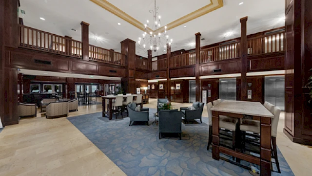 A spacious, elegant lobby with wood-paneled walls, comfortable seating, elevators, and a chandelier, offering a welcoming atmosphere.