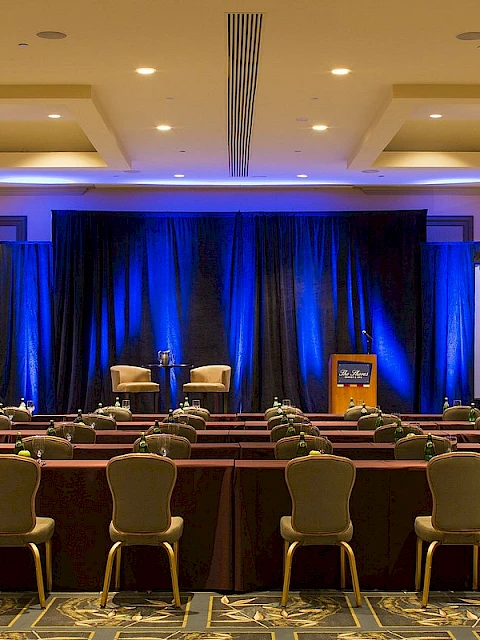 A conference room setup with chairs, tables, large screens, a podium, and chandeliers for an event or presentation.