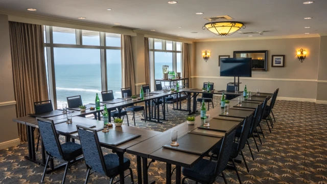 A conference room with a U-shape table setup, chairs, water bottles, glasses, and a view of the ocean through large windows.