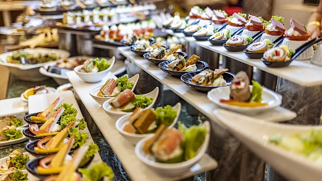 A variety of colorful appetizers and finger foods are displayed on a multi-tiered serving table at a buffet.