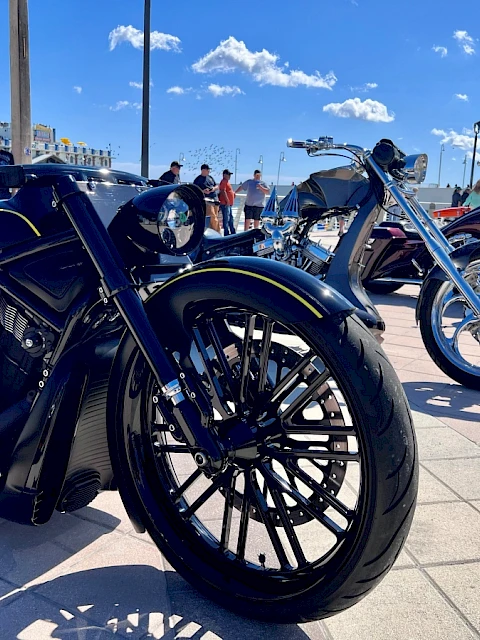 A lineup of custom and luxury motorcycles displayed outdoors on a sunny day at a bike show with people in the background.