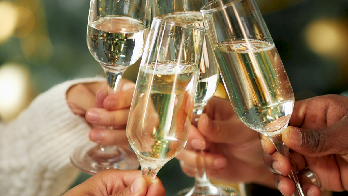 People are toasting with glasses of champagne in front of a festive background with blurred lights.