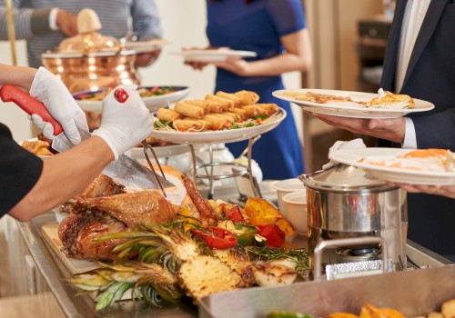 A buffet with carved meat, grilled vegetables, spring rolls, and people serving themselves from a selection of dishes.