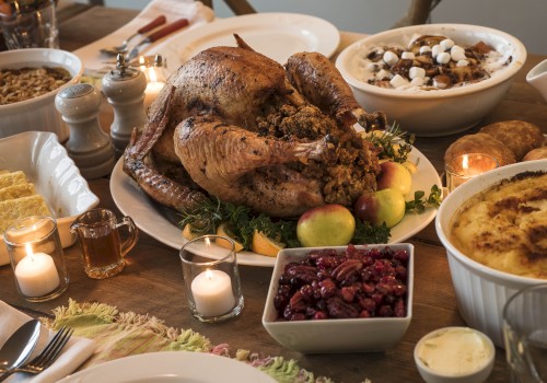 A festive dinner spread with a roasted turkey centerpiece, sides like stuffing, cranberry sauce, mashed dishes, candles, and desserts on a wooden table.