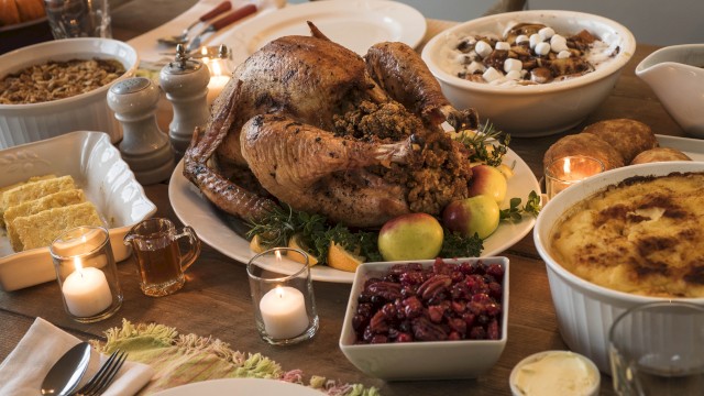 A festive dinner spread with a roasted turkey centerpiece, sides like stuffing, cranberry sauce, mashed dishes, candles, and desserts on a wooden table.