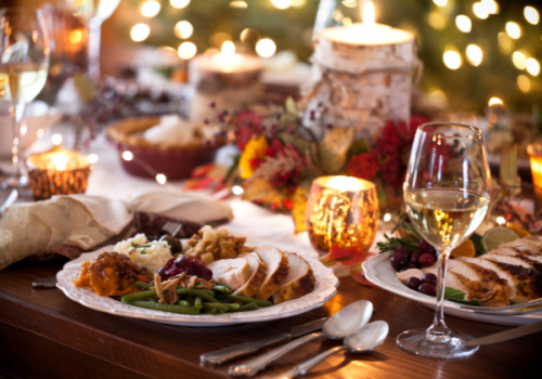 A festive dining table with plates of food, candles, wine glasses, and decorative elements, ready for a holiday meal.