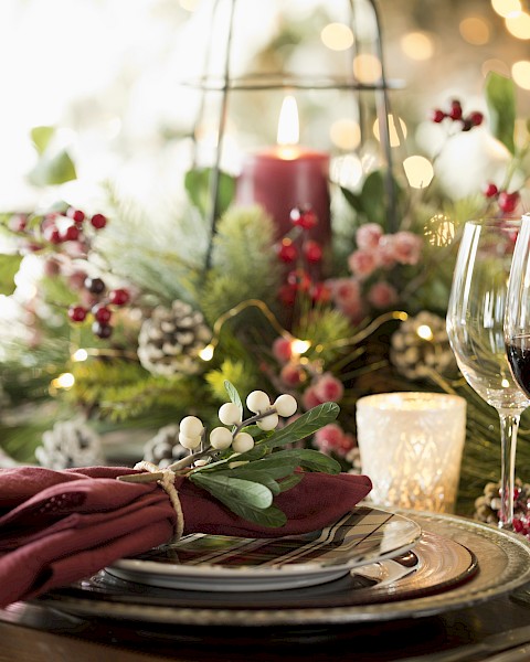 A festive table setting with wine glasses, candles, greenery, berries, and pinecones, creating a warm and elegant holiday atmosphere.