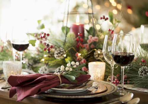 A festive table setting with wine glasses, candles, greenery, berries, and pinecones, creating a warm and elegant holiday atmosphere.