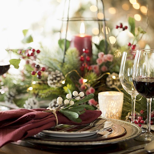 A festive table setting with wine glasses, candles, greenery, berries, and pinecones, creating a warm and elegant holiday atmosphere.