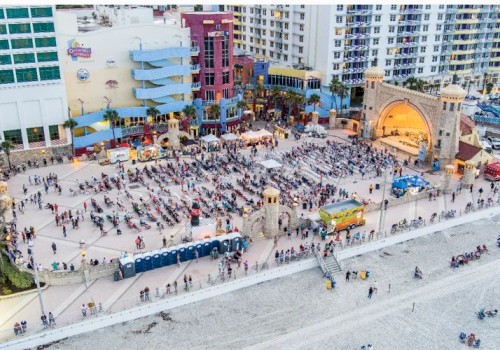 A crowded beach area near colorful buildings with many people sitting, walking, and enjoying time by the ocean.