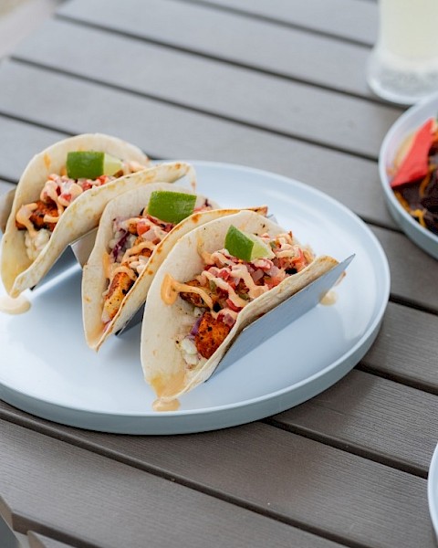 Three tacos filled with seasoned meat, cheese, and toppings, garnished with lime wedges on a white plate.