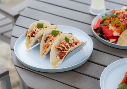 Three tacos filled with seasoned meat, cheese, and toppings, garnished with lime wedges on a white plate.