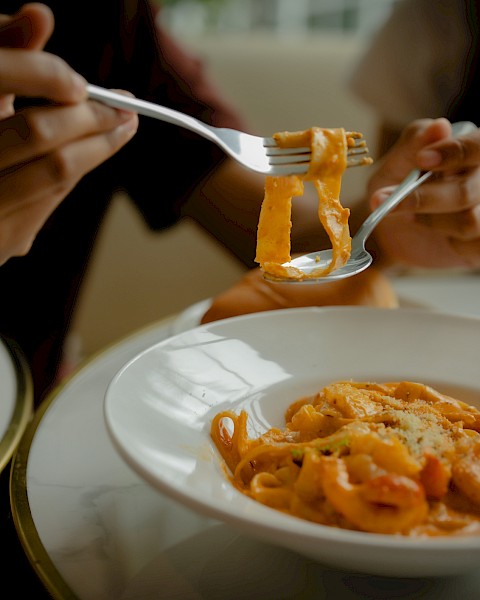 People eating spaghetti with forks, close-up shot showing action, sauce, and grated cheese.