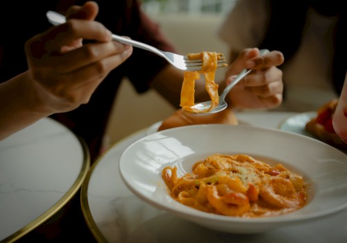 People eating spaghetti with forks, close-up shot showing action, sauce, and grated cheese.