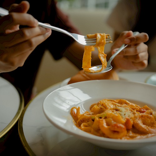 People eating spaghetti with forks, close-up shot showing action, sauce, and grated cheese.