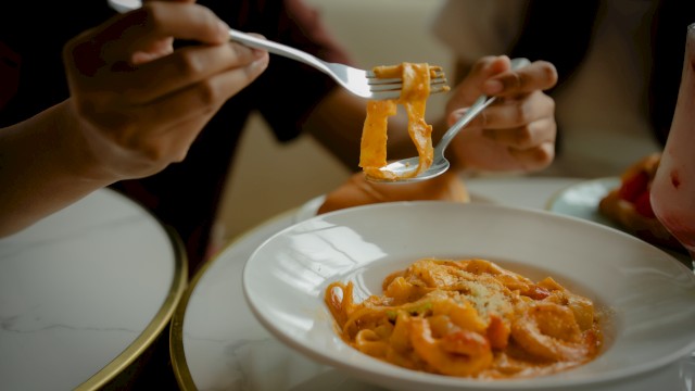 People eating spaghetti with forks, close-up shot showing action, sauce, and grated cheese.