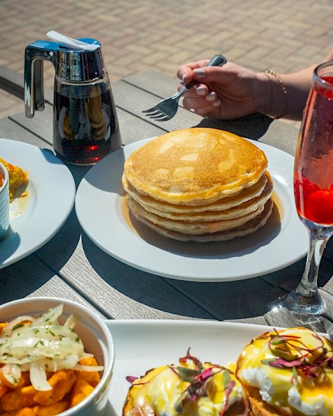 A table spread with pancakes, eggs Benedict, a salad, and drinks during breakfast outside.