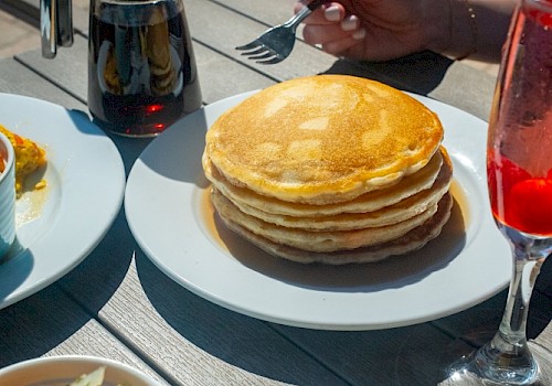 Una mesa preparada con panqueques, huevos Benedict, una ensalada y bebidas durante el desayuno al aire libre.
