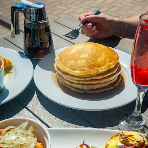 A table spread with pancakes, eggs Benedict, a salad, and drinks during breakfast outside.