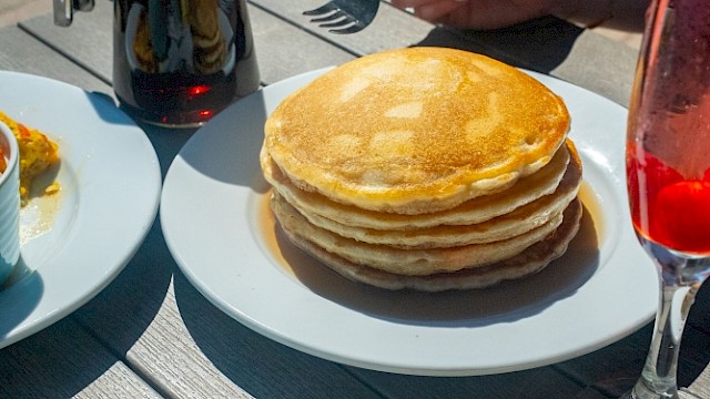 Una mesa preparada con panqueques, huevos Benedict, una ensalada y bebidas durante el desayuno al aire libre.