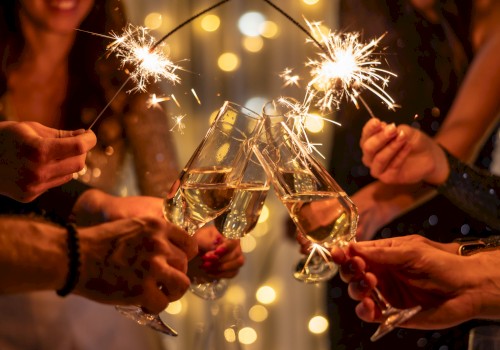 People toast with sparklers and champagne flutes, celebrating together under warm lights, cheers rising as they clink glasses.