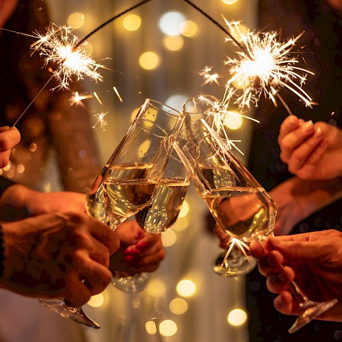People toast with sparklers and champagne flutes, celebrating together under warm lights, cheers rising as they clink glasses.
