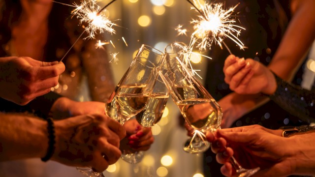 People toast with sparklers and champagne flutes, celebrating together under warm lights, cheers rising as they clink glasses.