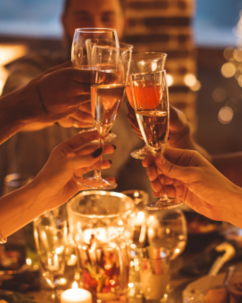 A group of people are toasting with champagne glasses at a festive, candle-lit table, creating a warm and celebratory atmosphere.