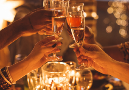 A group of people are toasting with champagne glasses at a festive, candle-lit table, creating a warm and celebratory atmosphere.