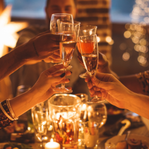 A group of people are toasting with champagne glasses at a festive, candle-lit table, creating a warm and celebratory atmosphere.