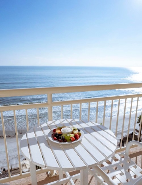 A balcony overlooking the ocean with a table of fruit and a scenic beach view at sunrise or sunset.