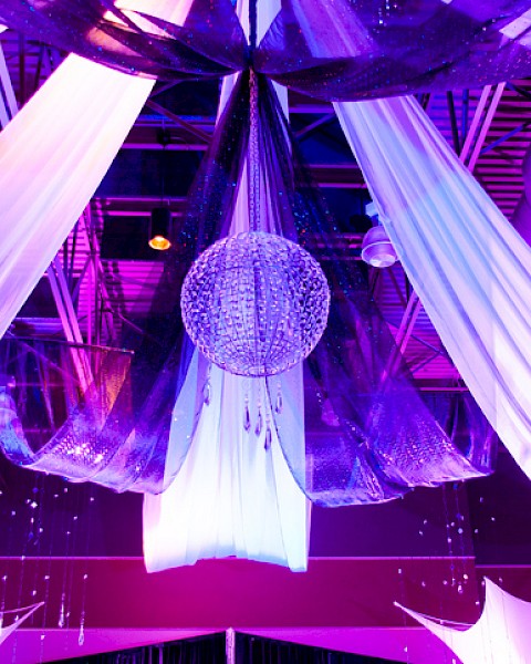 Colorful, illuminated event ceiling with drapes, a disco ball, and decorative fabric elements creating a festive atmosphere.