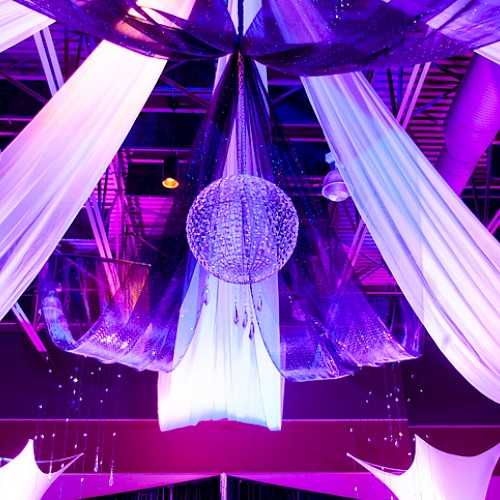 Colorful, illuminated event ceiling with drapes, a disco ball, and decorative fabric elements creating a festive atmosphere.