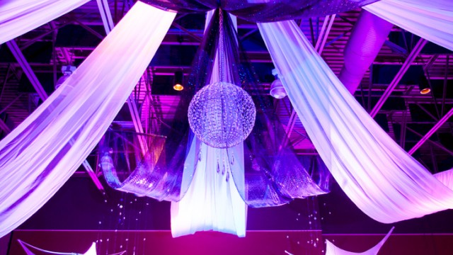 Colorful, illuminated event ceiling with drapes, a disco ball, and decorative fabric elements creating a festive atmosphere.