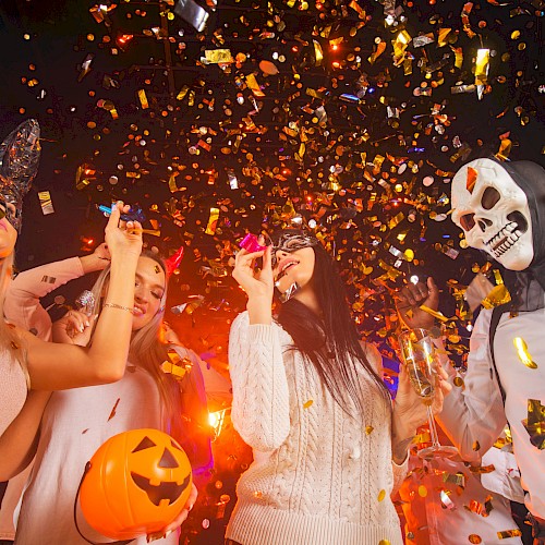 People celebrating Halloween at a party with costumes, masks, a pumpkin basket, and falling golden confetti.
