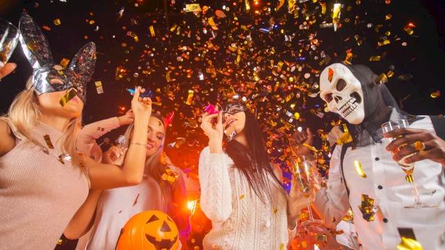 People celebrating Halloween at a party with costumes, masks, a pumpkin basket, and falling golden confetti.
