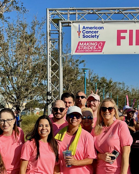 Group of people wearing pink shirts celebrating at a breast cancer awareness event near the finish line.