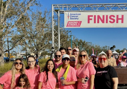 Group of people wearing pink shirts celebrating at a breast cancer awareness event near the finish line.