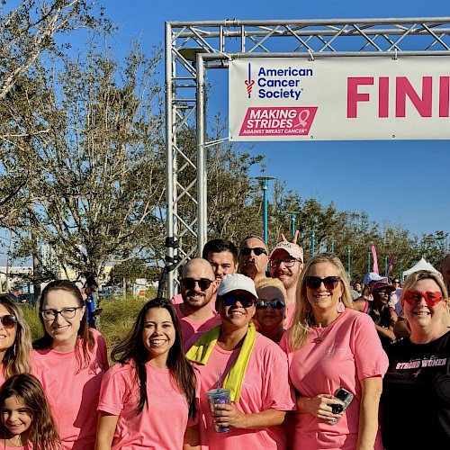 Group of people wearing pink shirts celebrating at a breast cancer awareness event near the finish line.