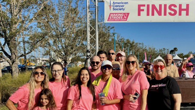 Group of people wearing pink shirts celebrating at a breast cancer awareness event near the finish line.
