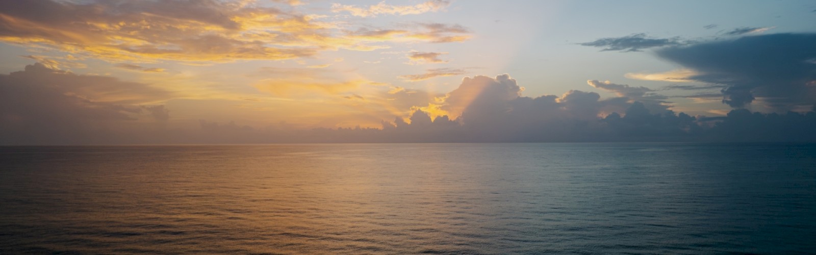 Sunset with orange hues over calm ocean waters, clouds dotting the horizon.