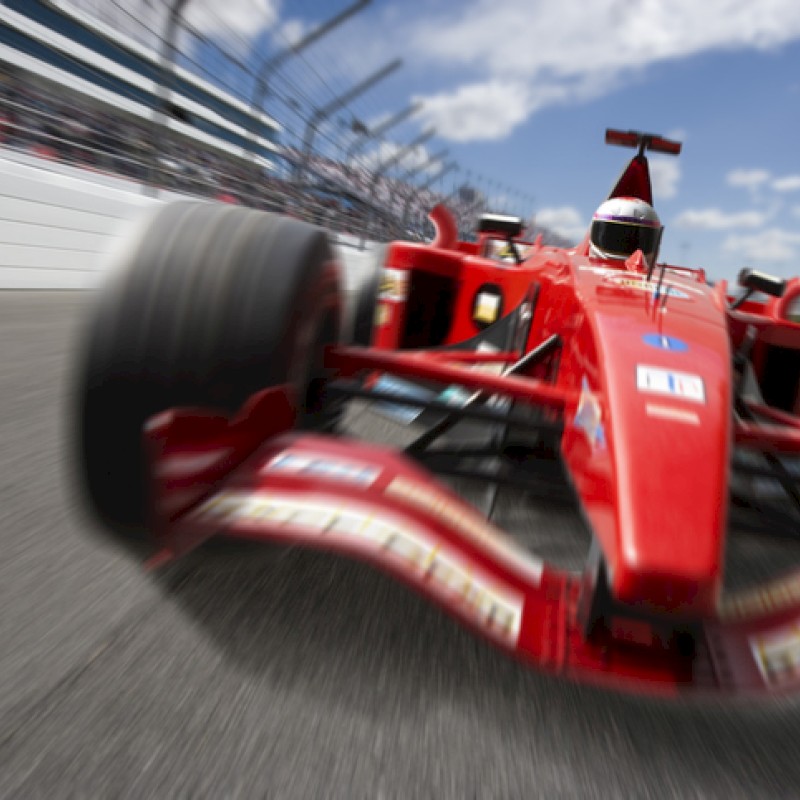 A red Formula 1 car is racing on the track with blurred tires and a clear blue sky in the background.