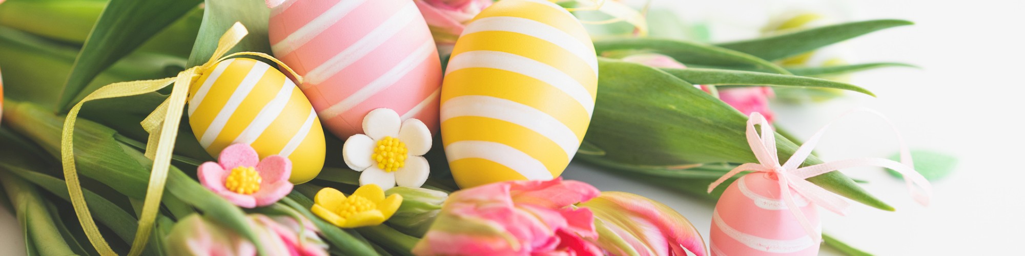 The image shows a bouquet of pink tulips adorned with striped Easter eggs and small decorative flowers on a light background.