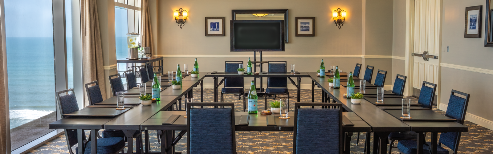 This is a conference room set up with tables, chairs, water bottles, glasses, and potted plants, ready for a meeting or presentation.
