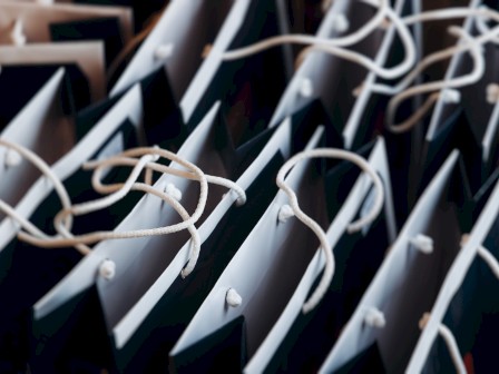 The image shows multiple black and white shopping bags with white handles arranged in rows.
